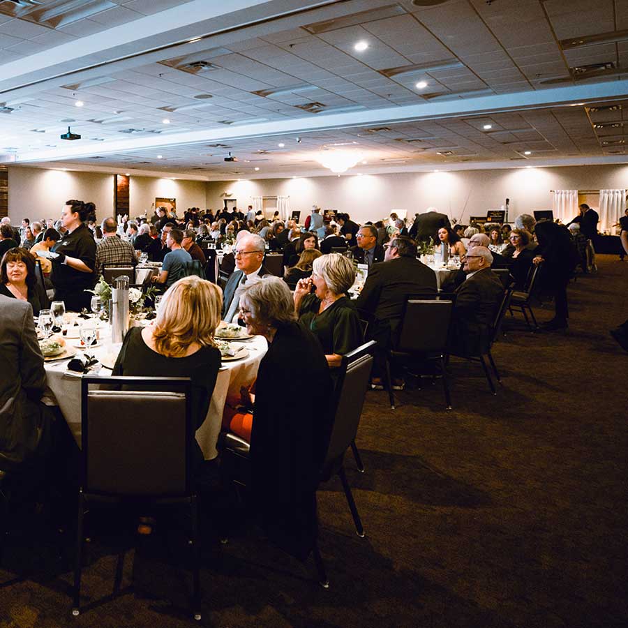 People seated at round tables in a large banquet hall during a formal event or dinner.
