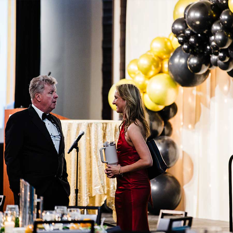 A man in a suit and woman in red chat at Special Events Rochester International Event Center.