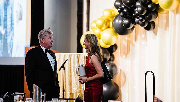 A man and woman talk near gold and black balloons at Rochester Event Center’s formal event.
