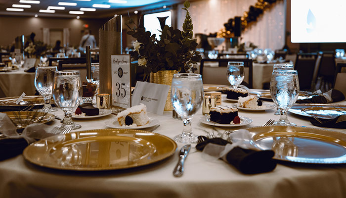 Elegant banquet table at Rochester Event Center set with gold plates, glasses, and cake slices.