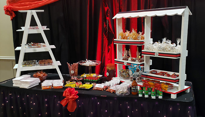 A decorated candy buffet at Rochester Event Center, with shelves of sweets and bags, red drapes behind.