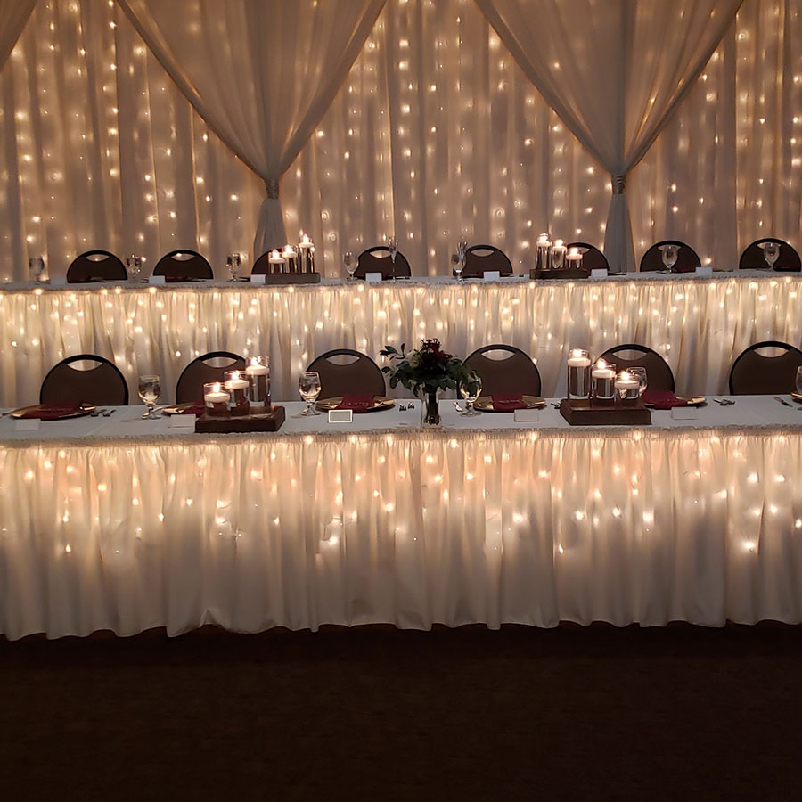 Wedding head table at Rochester Event Center with draped lights, candles—perfect for summer weddings.